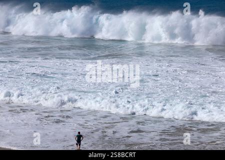 Homme debout au bord de l'eau regardant les vagues de surf écrasantes, Playa Piedra surf Beach, El Cotillo, Fuerteventura, îles Canaries, Espagne. Banque D'Images