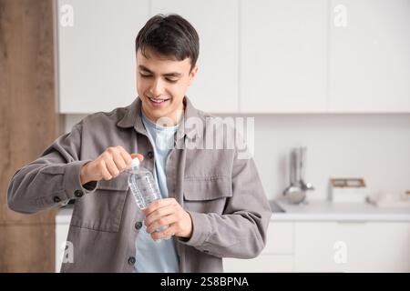 Beau jeune homme ouvrant une bouteille d'eau à la maison Banque D'Images