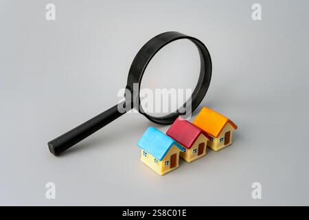 Une loupe et une maison de jouet sur un fond gris. Immobilier, recherche de propriété, achat de maison, ou concept d'investissement. Banque D'Images