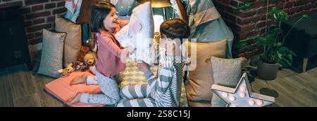 Bannière de frères et sœurs heureux s'amusant dans le combat d'oreiller au salon. Concept de vie familiale domestique. Banque D'Images