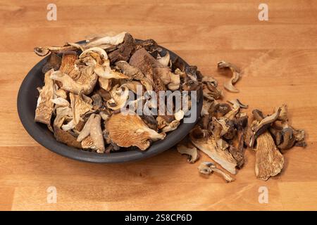Un bol brun rempli de champignons séchés, avec un petit tas de champignons se déversant sur une table wodden. Vue latérale. Banque D'Images