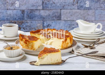 San Sebastian ou basque tranches de cheesecake brûlées sur plaque sur une table en bois blanc avec une tasse de café et de crème dans le fond de mur de briques, horizon Banque D'Images
