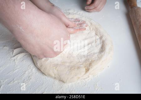 Les mains d'un homme et d'un enfant en farine font une tarte ou une pizza à partir de pâte. Le concept de relations familiales, de soutien et d'amour. Passer du temps ensemble Banque D'Images