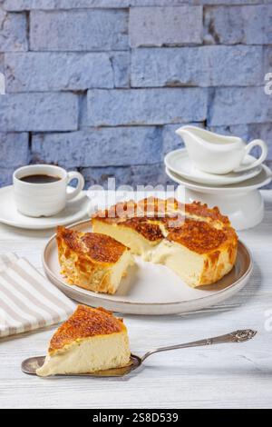 San Sebastian ou basque tranches de cheesecake brûlées sur l'assiette et sur la pelle à gâteau sur la table en bois blanc avec une tasse de café et de crème dans le fond de Banque D'Images