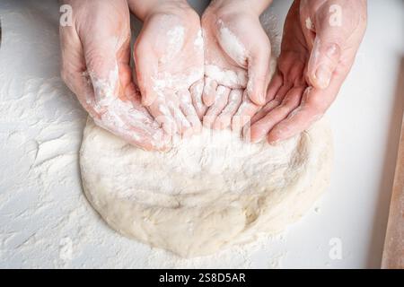 Les mains d'un homme et d'un enfant en farine font une tarte ou une pizza à partir de pâte. Le concept de relations familiales, de soutien et d'amour. Passer du temps ensemble Banque D'Images