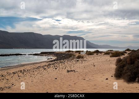 Couleur brun foncé à noir des falaises au nord de Lanzarote. Eau peu profonde d'une plage. Plage de sable. Ciel bleu avec des nuages blancs. Caleta del Sebo, Banque D'Images