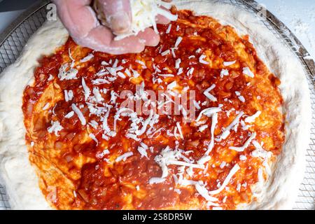Les mains des hommes saupoudrent de fromage sur la pizza. Le processus de fabrication de pizza Margherita avec des tomates. Photo de haute qualité Banque D'Images