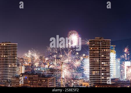 Des feux d'artifice vibrants illuminent le ciel nocturne au-dessus du centre-ville de Tbilissi, illuminant le paysage urbain avec des éclats colorés. Gratte-ciel et lumières urbaines offrent Banque D'Images
