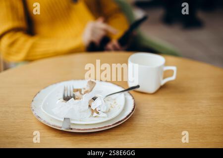 Un cadre de café confortable avec une table en bois avec une tasse et une assiette usagées serviettes en papier froissé ajoutent une touche vivante À Une personne dans un pull jaune Banque D'Images