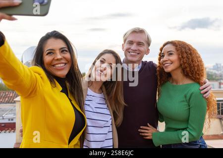 Un groupe d'amis joyeux prenant un selfie lors d'une fête dynamique, ils sourient largement, s'embrassent et apprécient la célébration en plein air Banque D'Images