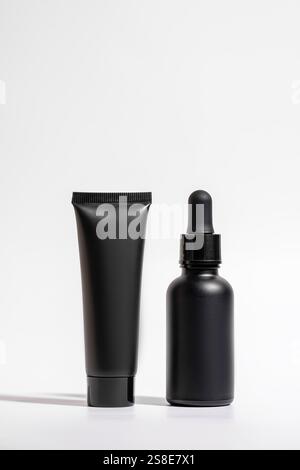 Élégant emballage cosmétique noir avec un tube et un flacon compte-gouttes isolés sur un fond blanc propre. Parfait pour présenter une skincar moderne Banque D'Images