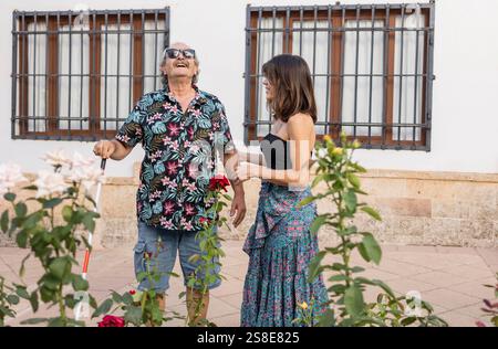 Un père aveugle handicapé explore une ville pittoresque, guidé par la main attentionnée de sa fille. Entouré de fleurs et d'architecture traditionnelle Banque D'Images