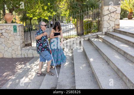 Un père aveugle, utilisant une canne blanche, monte un escalier carrelé à travers une ville accompagné et assisté de sa fille. Ils naviguent les escaliers et a si Banque D'Images