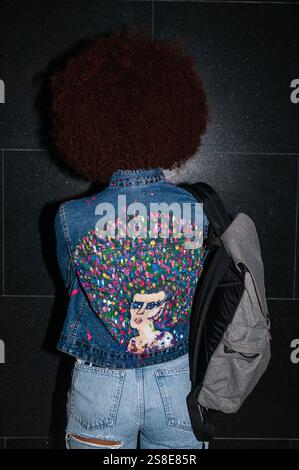 Vue arrière d'une femme africaine méconnaissable descendante avec cheveux afro. Elle porte une veste en denim décorée de façon unique et porte un sac à dos gris. Le s Banque D'Images