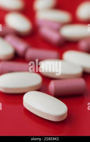 Une vue rapprochée de comprimés blancs et roses assortis dispersés sur un fond rouge vif, mettant en évidence les thèmes pharmaceutiques et les soins de santé. Banque D'Images