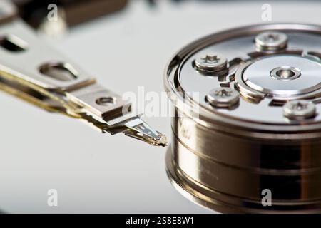 Gros plan détaillé montrant le bras de lecture-écriture d'un disque dur dans les détails précis, positionné au-dessus de la surface brillante du plateau. Banque D'Images
