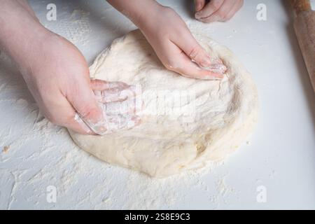 Les mains d'un homme et d'un enfant en farine font une tarte ou une pizza à partir de pâte. Le concept de relations familiales, de soutien et d'amour. Passer du temps ensemble Banque D'Images