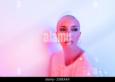 Une femme d'âge moyen avec une tête rasée est capturée dans un éclairage éclatant. Son expression confiante respire l'autonomisation et l'individualité contre un doux, Banque D'Images