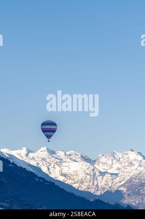 Une montgolfière colorée flotte gracieusement au-dessus des pittoresques sommets enneigés des Alpes, capturés sous un ciel bleu clair en journée, showcasi Banque D'Images