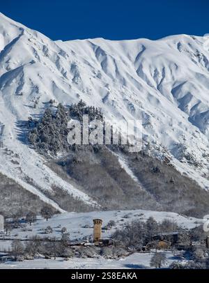 Une scène hivernale pittoresque avec des montagnes enneigées et une tour historique, entourée d'arbres givrés et d'un ciel bleu clair, capturant la sérénité Banque D'Images