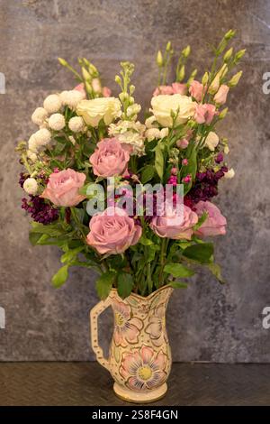 Bel arrangement de fleurs fraîches roses, blanches et violettes dans un vase artistique en céramique placé sur un comptoir, avec un dos texturé neutre Banque D'Images