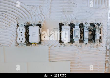 Plusieurs prises électriques, interrupteurs sont installés sur un mur texturé pendant les travaux de rénovation domiciliaire. Banque D'Images