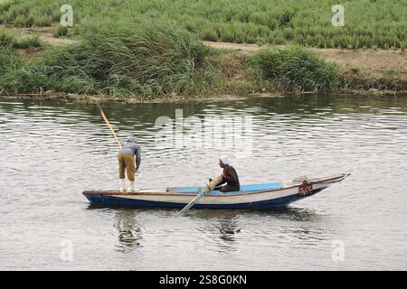 Nil, Egypte - mars 28 2015 deux hommes pêchant à partir d'un petit bateau. Une rangée et l'autre frappe l'eau pour effrayer les poissons dans leur filet. Banque D'Images