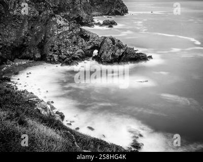 Falaises de granit accidentées, avec arche et mer floue longue exposition, sur la côte sud de Guernesey, îles Anglo-Normandes. Banque D'Images