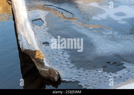 Lac partiellement gelé avec des motifs glacés à la surface formés par le gaz méthane émanant de bûches de bois pourries. Grotto Pond, Alberta, Canada. Banque D'Images