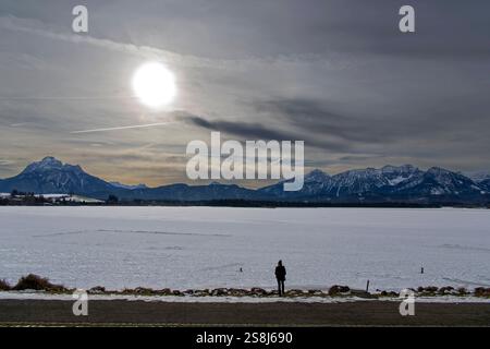 22.01.2025, Winterlandschaft BEI Füssen im Allgäu, Am Hopfensee. Die Promenade am Ufer des zugefrorenen See. Eine Frau steht an der Eisfläche. 22.01.2025, Winterlandschaft am Hopfensee BEI Füssen im Allgäu 22.01.2025, Winterlandschaft am Hopfensee BEI Füssen im Allgäu *** 22 01 2025, paysage hivernal près de Füssen im Allgäu, au lac Hopfensee la promenade au bord du lac gelé Une femme se dresse sur la glace 22 01 2025, paysage hivernal au lac Hopfensee près de Allgäu im Füssen 22 01 2025, paysage hivernal au lac Hopfensee près de Füssen im Allgäu Banque D'Images