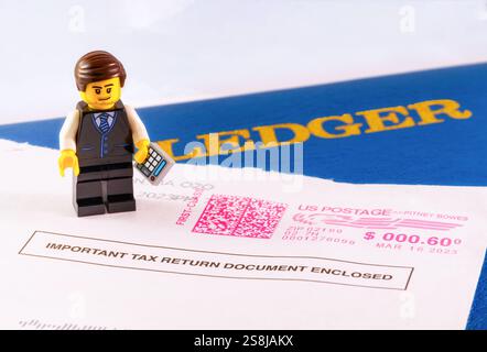 Chappaqua, NY - 11 avril 2024 : concept de jour de l'impôt sur le revenu Lego minifigure comptable avec livre de grand livre et enveloppe IRS marqué d'importantes informations fiscales Banque D'Images