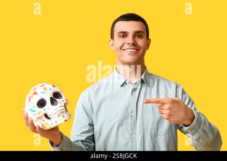 Beau jeune homme pointant le crâne peint sur fond jaune Banque D'Images