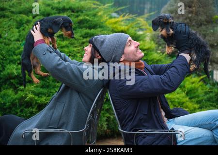 Couple soulevant des chiens de teckel tout en étant assis dos à dos sur des chaises dans le jardin Banque D'Images
