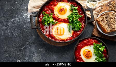 Oeufs Shakshuka dans une casserole avec du pain sur un fond sombre. Oeufs pochés dans une sauce épicée au poivre tomate. Œufs brouillés juifs traditionnels. Vue de dessus. Co Banque D'Images