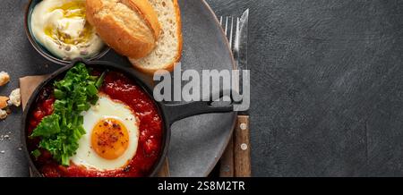 Oeufs Shakshuka dans une casserole avec du pain sur un fond sombre. Oeufs pochés dans une sauce épicée au poivre tomate. Œufs brouillés juifs traditionnels. Vue de dessus. PA Banque D'Images