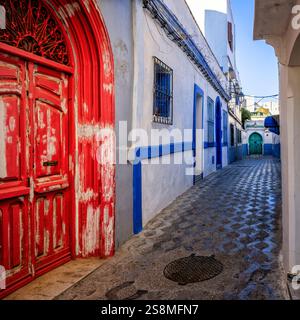 Ruelle colorée à l'intérieur de l'Asilah ou Assilah Medina, Maroc. Petite ville marine coloniale marocaine dans la province de Tanger. Belle porte rouge en bois. Banque D'Images
