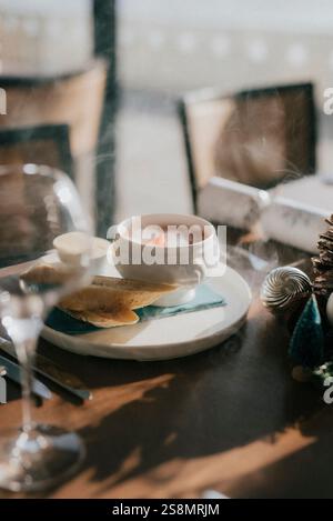 Un bol blanc de soupe repose sur une assiette sur une table. La table est sertie avec un verre à vin, une fourchette et un couteau. La soupe est accompagnée de pain, et là Banque D'Images