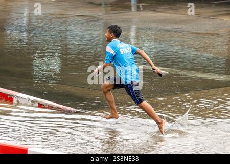 SAMUT PRAKAN, THAÏLANDE, SEP 25 2024, garçon pieds nus courant dans une flaque d'eau dans la rue Banque D'Images