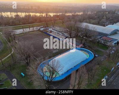 Vue aérienne d'une patinoire, d'un terrain de football et d'autres installations sportives à côté du fleuve po qui coule à Crémone, en Italie, pendant le coucher du soleil en hiver Banque D'Images