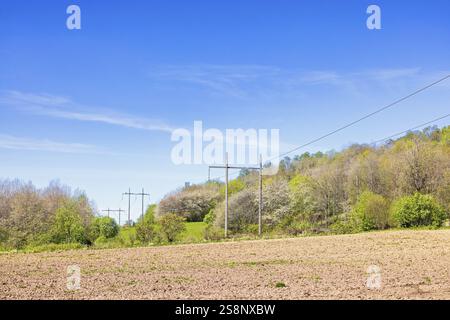 Powerline sur un champ avec de la terre arable sèche par une forêt feuillus verdoyante une journée de printemps ensoleillée dans la campagne, Suède, Europe Banque D'Images