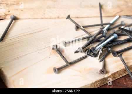 Une collection de diverses vis dispersées sur une surface en bois, y compris des vis noires et des boulons argentés, avec un objet métallique triangulaire parmi eux. Banque D'Images