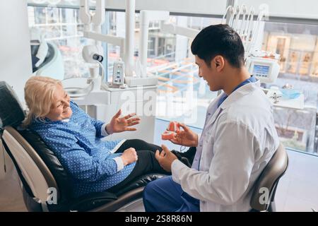 Jeune professionnel, dentiste montre des prothèses dentaires, expliquant les options au patient attentif dans le cabinet dentaire moderne et lumineux Banque D'Images
