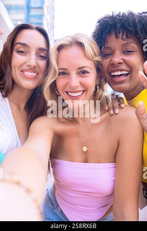 Trois jeunes femmes heureuses prenant un selfie ensemble dans une rue de la ville. Vertical Banque D'Images