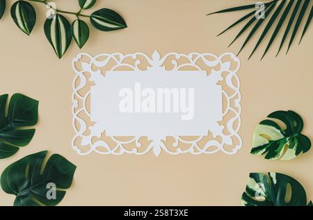 Composition d'été à la mode faite avec des feuilles tropicales vertes et une note de carte de papier sur fond de couleur sable. Concept minimal. Pose à plat exotique. Banque D'Images