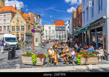 Bruges, Belgique, le 5 juillet 2023 : les gens traînent assis passent du temps dans le restaurant de rue et les cafés sur la place du marché aux œufs Eiermarkt avec un vieux bâtiment coloré Banque D'Images