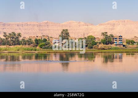 Une paisible ville riveraine de Naqadah en Égypte, avec des bâtiments traditionnels et une végétation luxuriante, avec le désert du Sahara derrière Banque D'Images