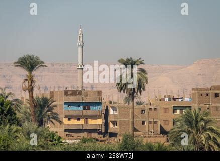 Une paisible ville riveraine de Naqadah en Égypte, avec des bâtiments traditionnels et une végétation luxuriante, avec le désert du Sahara derrière Banque D'Images