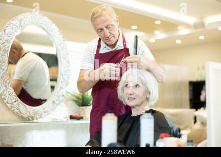 Le maître expérimenté de l'homme senior fait effectue la coupe de cheveux pour la femme mature avec des ciseaux Banque D'Images