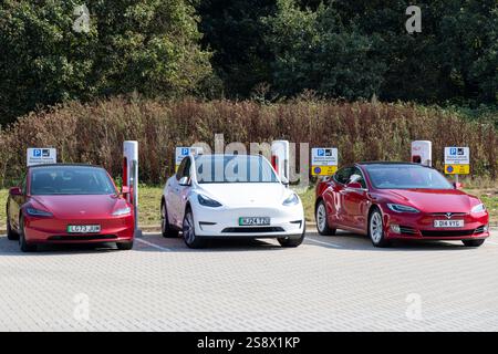 Tels Model 3, Tesla Model y et Tesla Model 3 en rouge et blanc garés ensemble sur des chargeurs de voitures électriques publics en Angleterre, au Royaume-Uni, 2024 Banque D'Images