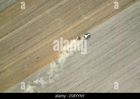 Vue aérienne d'un tracteur cultivant en hersant un large champ agricole, le préparant pour le prochain semis. Banque D'Images
